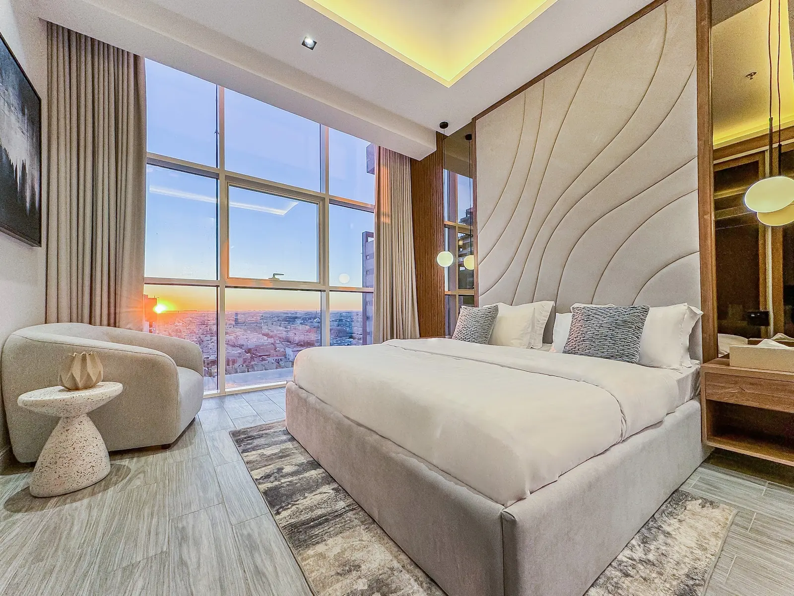 Master bedroom with a sculpted headboard, armchair and floor-to-ceiling windows