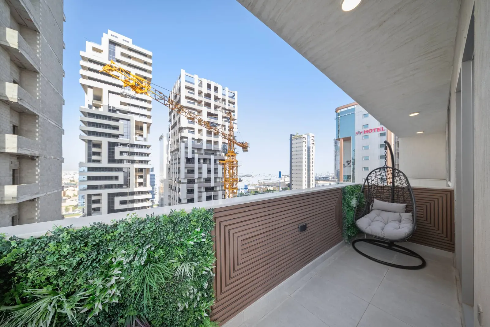 Wraparound balcony with a hanging chair, green wall and a view of the KAFD towers