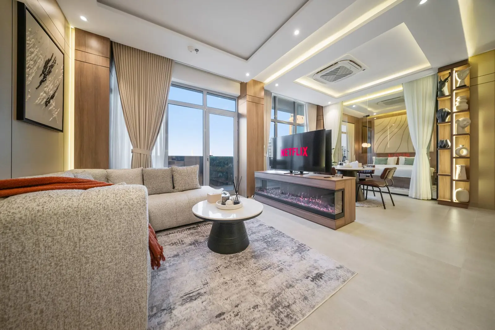 Living room with a sofa, electric fireplace under the TV, display wall and city windows