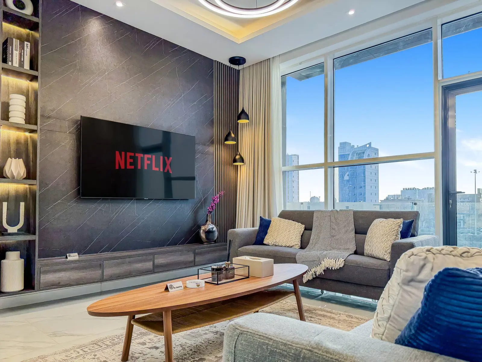 Living room with a smart TV wall, sofa and coffee table in front of tall windows