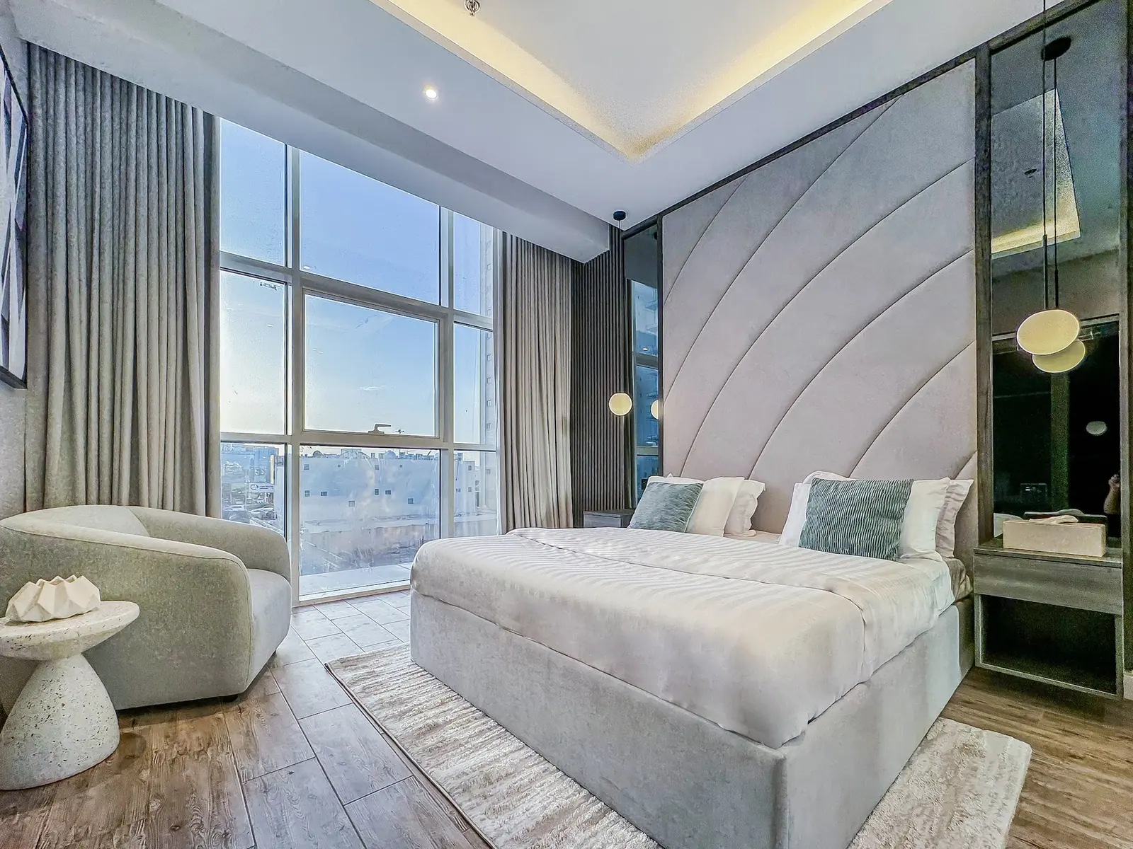 Master bedroom with a sculpted headboard, armchair and floor-to-ceiling windows