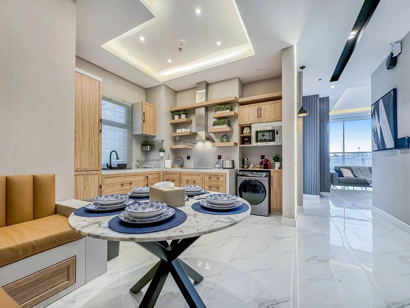 Kitchen with light wood cabinets, a washer-dryer and a dining nook with a leather banquette