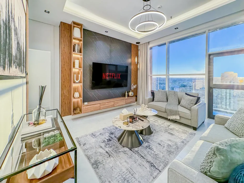 Daytime living room with floor-to-ceiling window, curated shelves, and plush seating inside a high-floor furnished apartment with balcony.